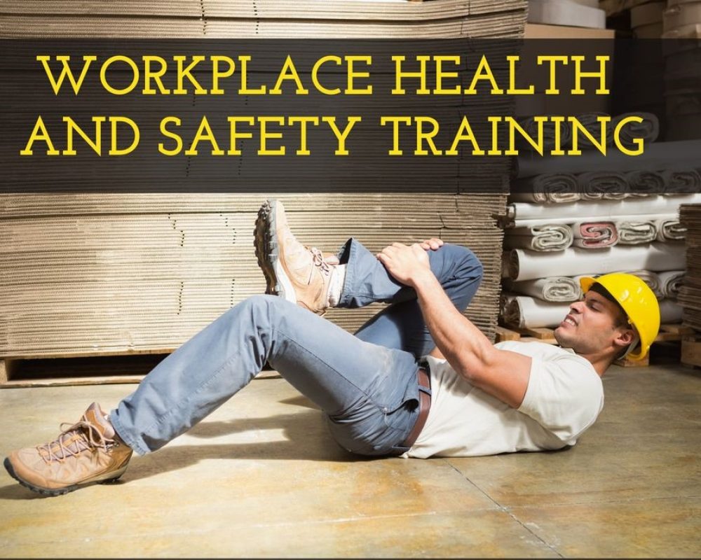 Warehouse worker in a yellow hard hat performs a floor exercise as part of workplace health and safety training in a stacks-and-pallets setting.